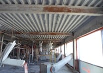Untitled construction site with machinery and building materials under a corrugated metal roof.